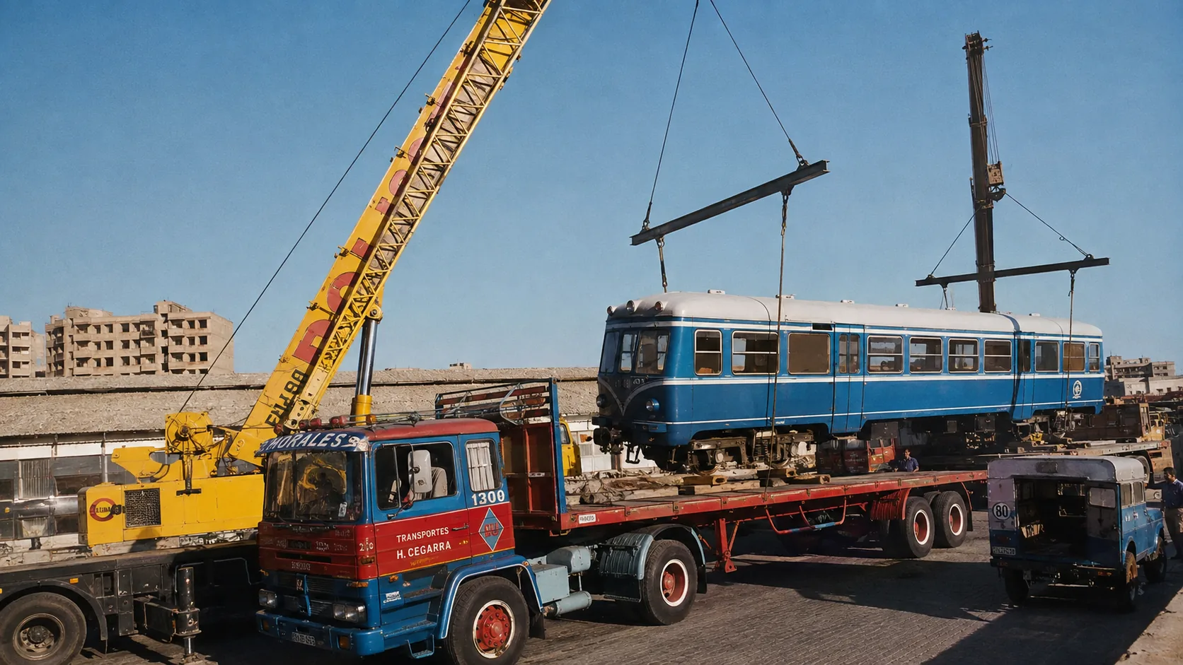 Grúa amarilla de Polisol izando un automotor ferroviario azul sobre una góndola de transporte especial